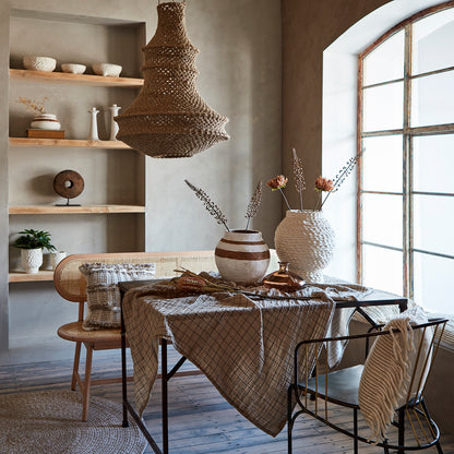 En beige bordsduk med svart rutmönster, omgiven av trendiga och snygga urnor och torkade blommor på ett matbord.